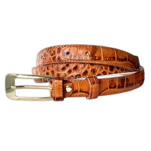 May include: A brown leather belt with a crocodile skin texture. The belt has a gold-coloured buckle and a matching leather loop. The belt is rolled up, showing the texture and colour variations. The belt is approximately 3.2 cm wide.