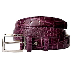 May include: A deep purple belt featuring a textured crocodile skin pattern. The belt includes a polished silver-tone rectangular metal buckle and a small metal tag near the buckle that reads Made in Italy. The strap has visible adjustment holes.