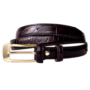 Peut inclure: Une ceinture bordeaux foncé présentant un motif gaufré façon crocodile sur toute la longueur de la sangle. La ceinture est fixée par une boucle rectangulaire en métal doré poli et un rivet en métal doré assorti sur le passant.
