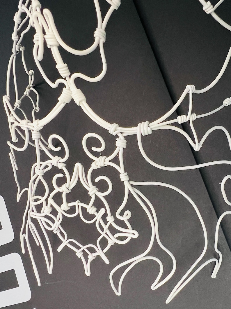 May include: A white, wire-sculpted decorative piece with intricate, swirling designs. The artwork features a network of curved lines and knots, creating a delicate, openwork pattern. The piece is set against a dark background, highlighting its form.