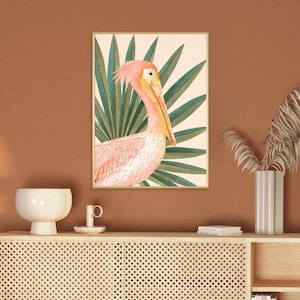 May include: A framed print of a pink pelican with a long beak standing in a tropical green palm leaf setting.