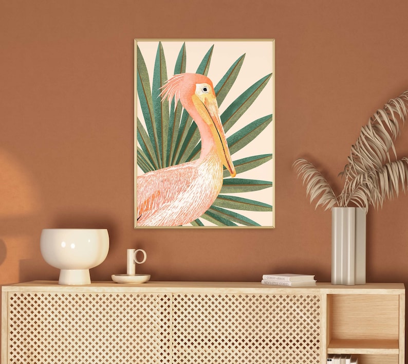 May include: A framed print of a pink pelican with a long beak standing in a tropical green palm leaf setting.