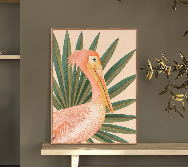 May include: A pink and orange pelican with a long beak stands in front of a green palm leaf background. The pelican is facing the right side of the image. The background is a light peach color.