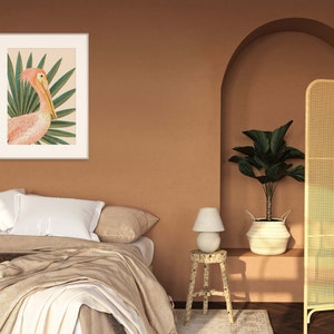May include: A framed print of a pink pelican with a tropical leaf background. The print is hanging on a wall in a room with a bed, a lamp, and a plant.