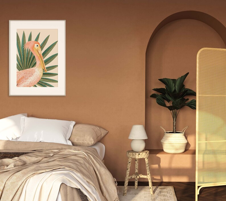 May include: A framed print of a pink pelican with a tropical leaf background. The print is hanging on a wall in a room with a bed, a lamp, and a plant.