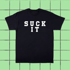 以下が含まれることがあります： 白い文字で「SUCK IT」と書いてある黒いTシャツ。太字でブロック体です。