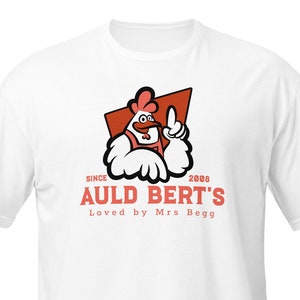 Puede incluir: Camiseta blanca con un logotipo rojo y naranja que presenta un gallo de dibujos animados y el texto "Since 2008 Auld Bert's Loved by Mrs. Begg"