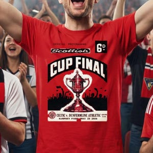 Op de afbeelding: Een menigte enthousiaste sportfans viert een overwinning. Een man in het midden draagt een rood t-shirt met de tekst "Scottish Cup Final" en een trofee-afbeelding. Fans dragen sjaals en zwaaien met vlaggen, confetti valt van boven.