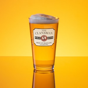 Puede incluir: Un vaso de cerveza con una cabeza blanca en un vaso de pinta transparente. El vaso tiene una etiqueta que dice "The Clansman Public House Pride of Craiglang - Glasgow -."