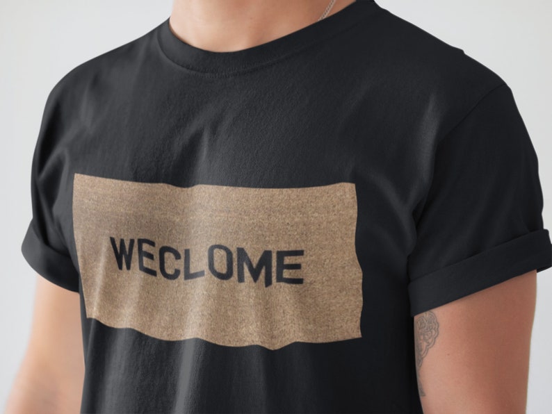 May include: A black t-shirt with a brown rectangle featuring the text "WECLOME" in black.