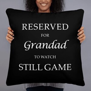 May include: Black throw pillow with white text that reads "RESERVED FOR Grandad TO WATCH STILL GAME".