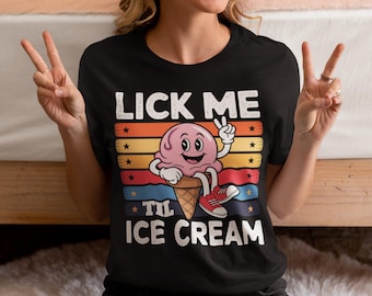 Op de afbeelding: Zwart T-shirt met een kleurrijke afbeelding van een ijsje. De tekst "LICK ME 'TIL ICE CREAM" staat boven en onder het ijsje. Het ijsje is roze en draagt rode sneakers.