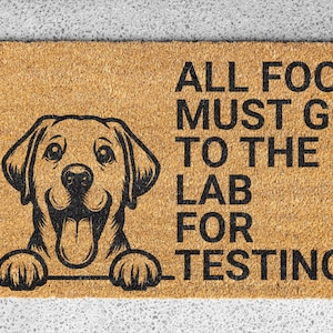 Puede incluir: Una alfombra rectangular con un fondo marrón claro y una ilustración en negro de un perro Labrador Retriever. El texto "ALL FOOD MUST GO TO THE LAB FOR TESTING" está impreso en negro.