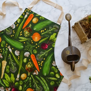 May include: A green apron with a colourful vegetable print. The apron has adjustable straps and a large pocket. The apron is ideal for gardening or cooking.