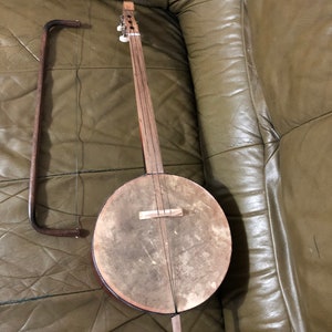 Puede incluir: Un instrumento musical de madera con un cuerpo redondo y un cuello largo. El instrumento tiene una sola cuerda y un arco de madera.