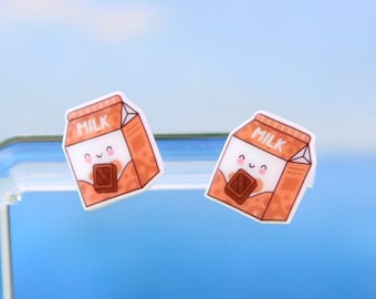 Könnte beinhalten: Ein Paar Ohrringe in Form eines Schokoladenmilchkartons mit einem niedlichen Comic-Gesicht und dem Wort "MILCH" auf der Vorderseite.