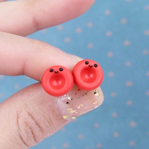 May include: A pair of red clay earrings with a smiley face design. The earrings are small and have a simple, minimalist style.