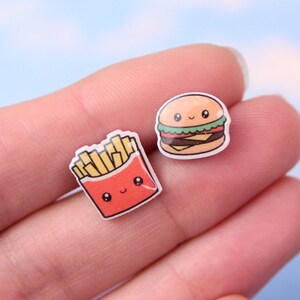May include: A pair of earrings featuring a cartoon burger and a cartoon box of french fries. Both have cute faces.
