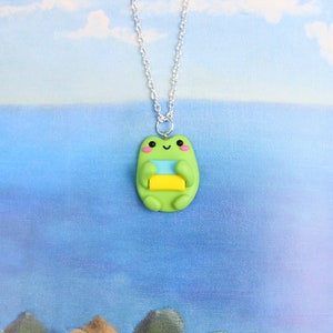 May include: A green frog charm necklace with a light blue and yellow stripe pattern. The frog is smiling and has pink cheeks.