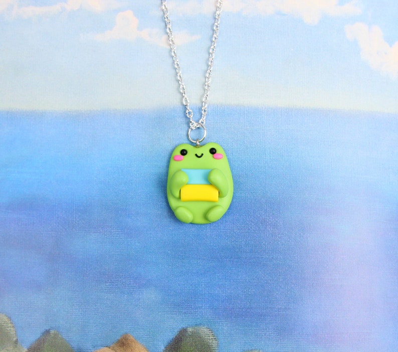 May include: A green frog charm necklace with a light blue and yellow stripe pattern. The frog is smiling and has pink cheeks.