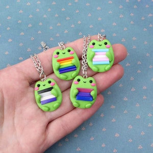 Puede incluir: Cuatro collares de rana verde con diferentes colores de banderas del arco&iacute;ris. Cada rana sostiene una pila de rayas de colores que representan a la comunidad LGBTQ+.