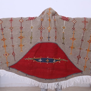 May include: A large, round, gray rug with a red and blue geometric design in the center. The rug has white fringe around the edges.