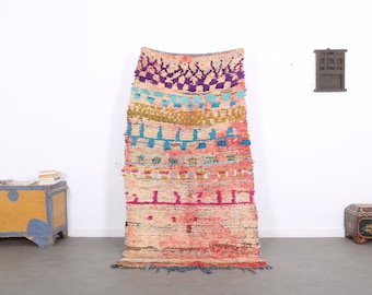 May include: A colourful Moroccan rug with a geometric pattern in shades of pink, blue, green, and purple. The rug is woven with a thick, textured yarn and has a fringe on the bottom.