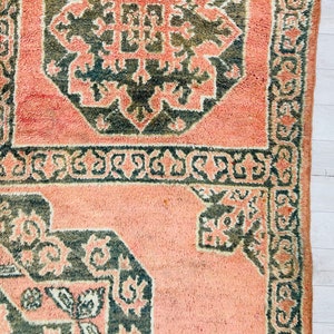 May include: A pink and green patterned rug with a geometric design. The rug has a fringe border.