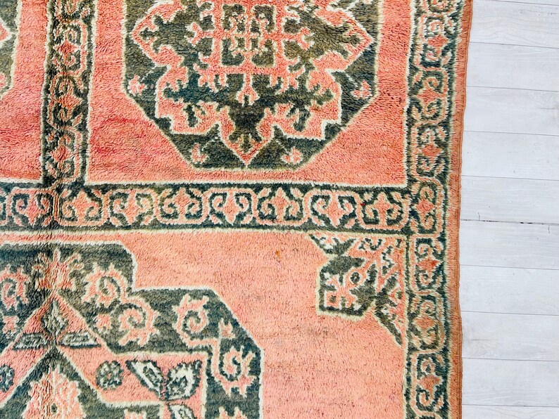 May include: A pink and green patterned rug with a geometric design. The rug has a fringe border.