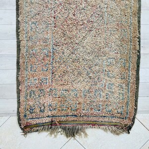 May include: A vintage rug with a faded floral pattern in shades of blue, red, and beige. The rug has a fringe border and is worn with age.
