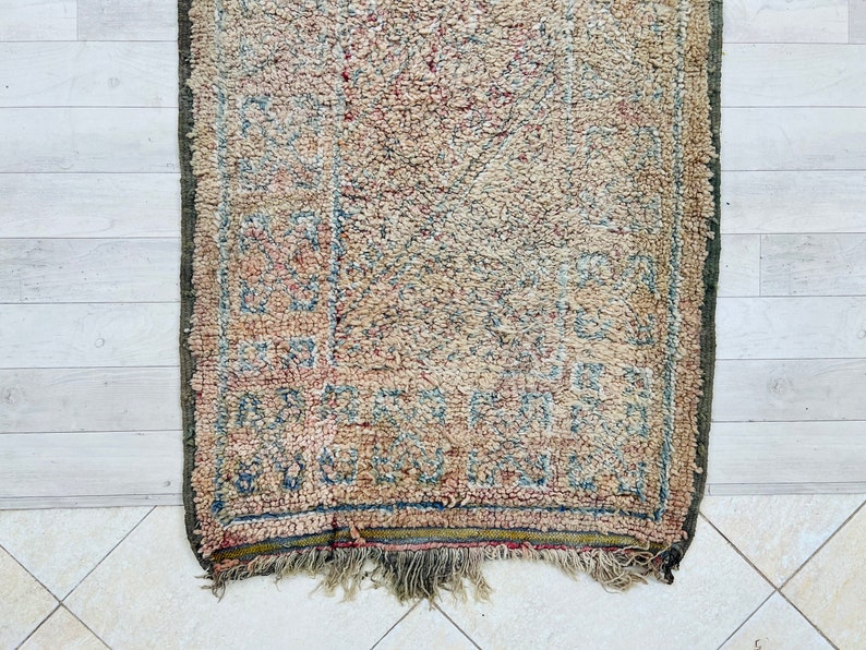 May include: A vintage rug with a faded floral pattern in shades of blue, red, and beige. The rug has a fringe border and is worn with age.