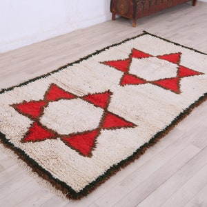 K&ouml;nnte beinhalten: Ein wei&szlig;er Teppich mit zwei roten und braunen Sternmotiven. Der Teppich hat einen gr&uuml;nen Rand und ist aus einem flauschigen Material gefertigt.