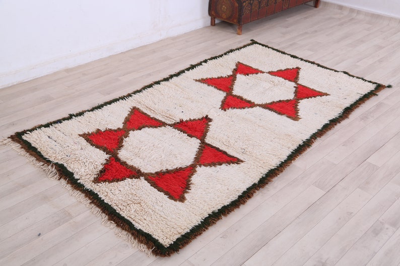 K&ouml;nnte beinhalten: Ein wei&szlig;er Teppich mit zwei roten und braunen Sternmotiven. Der Teppich hat einen gr&uuml;nen Rand und ist aus einem flauschigen Material gefertigt.