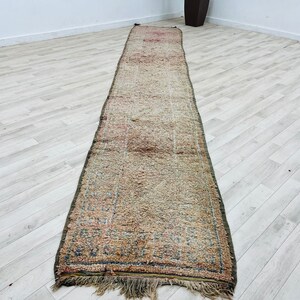 May include: A long, rectangular rug with a faded, vintage look. The rug has a cream background with a subtle pattern of pink, blue, and green. The rug has a fringe border.