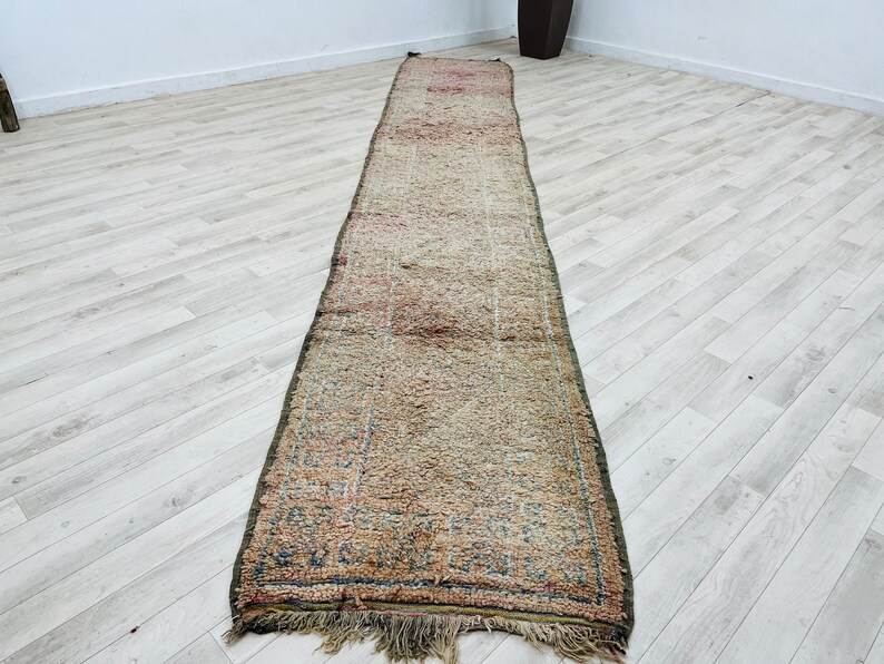 May include: A long, rectangular rug with a faded, vintage look. The rug has a cream background with a subtle pattern of pink, blue, and green. The rug has a fringe border.