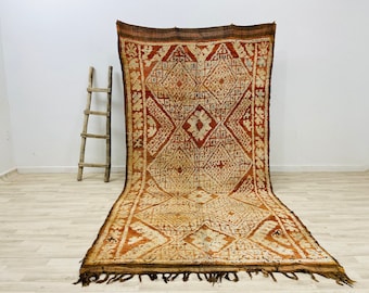 May include: A vintage Moroccan rug with a geometric pattern in shades of brown, orange, and white. The rug has a fringe border and is woven with a traditional technique.