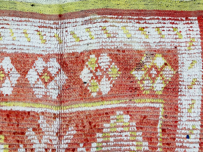 Puede incluir: Primer plano de una alfombra roja, blanca y amarilla con un dise&ntilde;o tejido texturizado. La alfombra tiene un patr&oacute;n repetitivo de flores.