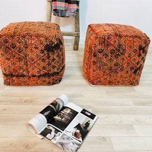 K&ouml;nnte beinhalten: Zwei quadratische, orange-braune Poufs mit einem Magazin auf dem Boden davor.