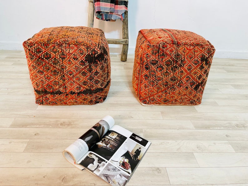 K&ouml;nnte beinhalten: Zwei quadratische, orange-braune Poufs mit einem Magazin auf dem Boden davor.
