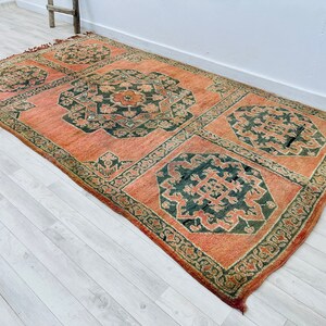 May include: A vintage rug with a traditional Persian design. The rug has a peach background with dark green and black floral patterns.