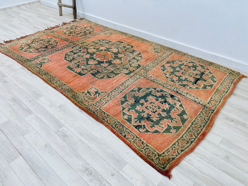 May include: A vintage rug with a traditional Persian design. The rug has a peach background with dark green and black floral patterns.