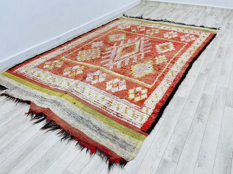 Puede incluir: Una alfombra roja, blanca y negra con un dise&ntilde;o geom&eacute;trico. La alfombra tiene un borde de flecos y est&aacute; hecha de lana.