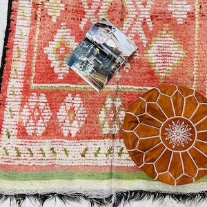 Puede incluir: Una alfombra roja y blanca con un patr&oacute;n con un puf de cuero marr&oacute;n con costuras blancas. Una revista est&aacute; sobre la alfombra.