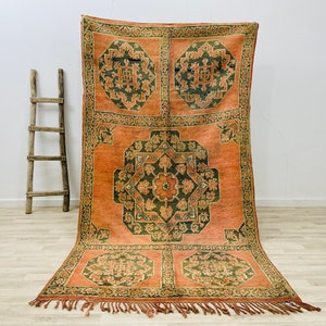 May include: A vintage rug with a geometric pattern in shades of orange, green, and brown. The rug has a fringe border and is made of wool.