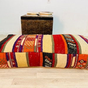 May include: A colorful, striped, woven floor cushion with a geometric pattern. The cushion is made of a thick, durable fabric and is perfect for adding a touch of bohemian style to any room.