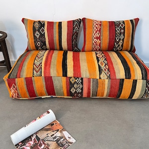 May include: A colorful, striped floor cushion with two matching pillows. The cushion and pillows are made of woven fabric with a traditional pattern.