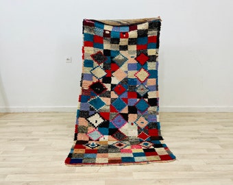 May include: A colourful Moroccan rug with a geometric pattern of squares and diamonds in shades of red, blue, black, and white.
