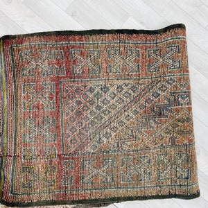 May include: A vintage rug with a geometric pattern in shades of red, brown, and beige. The rug has a fringe border and is made of wool.
