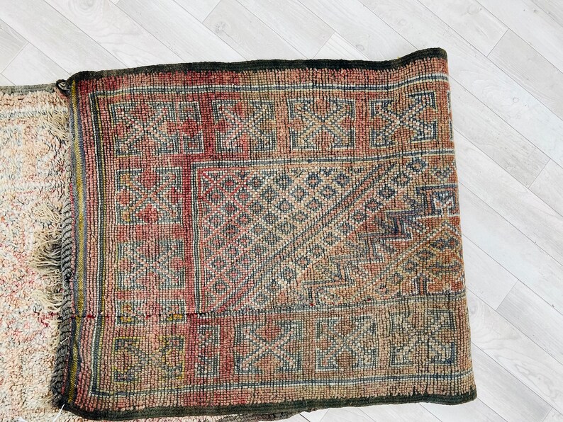 May include: A vintage rug with a geometric pattern in shades of red, brown, and beige. The rug has a fringe border and is made of wool.