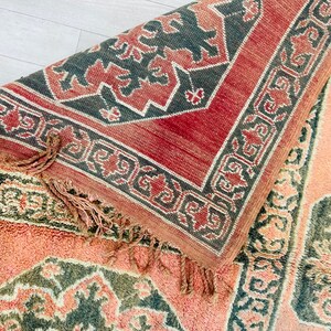 May include: A close-up of a pink and green patterned rug with a fringe. The rug has a geometric design with a central medallion.